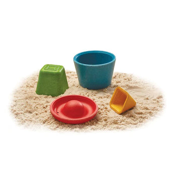 PlanToys Creative Sand Play set includes colorful plastic molds: green cube, red dome, blue cylinder, and yellow cone on white sand.