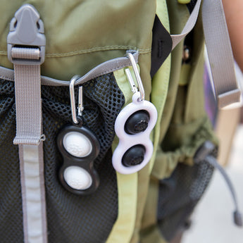 A black and white Simpl Dimpl from Fat Brain Toy Co offers tactile stimulation in a green backpacks gray mesh pocket.