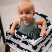 A baby sits in a patterned basket, wrapped snugly in a Milk Snob Cover Disneys Mickey Mouse, wearing a gray outfit, and looks up curiously.