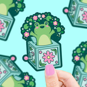 Turtle Soups Frog Jack In The Box vinyl sticker is waterproof and durable, featuring a green frog with a floral afro.