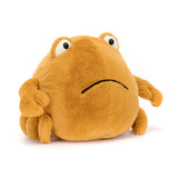 A round Jellycat plush, Chrissie Crab, with big eyes and small frown sits on white background, boasting a soft tangerine shell.