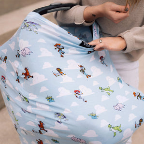 Someone adjusts a Milk Snob Cover Disney & Pixars Toy Story on a light blue baby stroller, ideal for 360° nursing coverage outdoors.