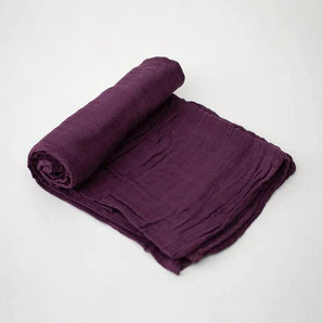 A rolled-up Cotton Swaddle in Plum by Little Unicorn on a light gray background.