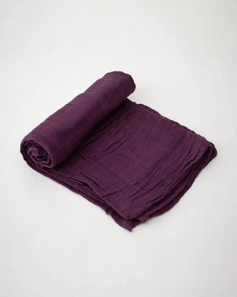 A rolled-up Cotton Swaddle in Plum by Little Unicorn on a light gray background.