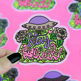 The Turtle Soup Stay Weird vinyl sticker features vibrant text, a hat, roses, hearts, and greenery held by a hand with black nails.