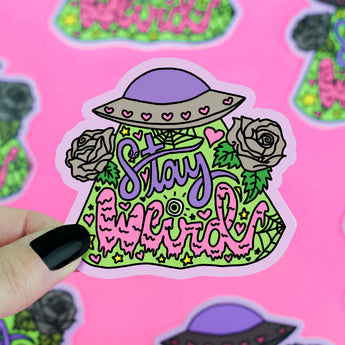 The Turtle Soup Stay Weird vinyl sticker features vibrant text, a hat, roses, hearts, and greenery held by a hand with black nails.