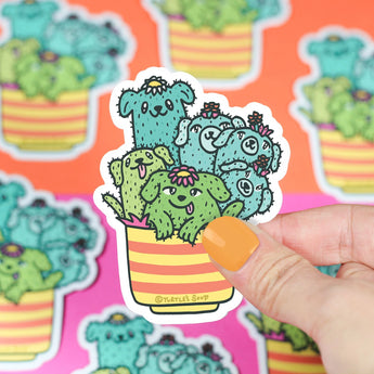 Hand holds a Turtle Soup Vinyl Sticker, Cactus Pups design; cute and durable with more premium vinyls in the background.
