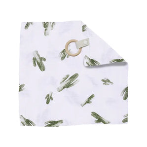 The Bebe Au Lait Muslin Teether Blanket features a white burp cloth with green cactus prints and a tan wood teether in one corner.