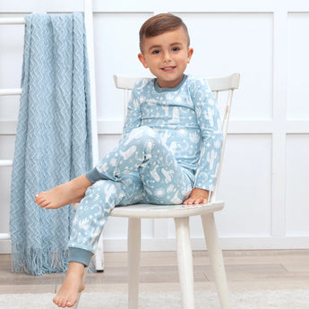 A child smiles in Tesa Babes Wild West Blue PJs while a textured blue blanket drapes over a nearby ladder.