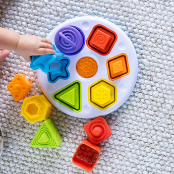 Child develops fine motor skills with the colorful Plugzy Shape Learning Toy by Fat Brain Toy Co, featuring circles, stars, triangles & squares.