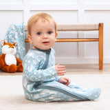 A baby in Tesa Babes Wild West Blue romper sits on a light carpet, with a charming fox plush toy in the background.