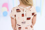A child wearing the comfy, lightweight Blake Birdie Dress by Birdie Bean, featuring chocolate cake patterns and a bow-tied back.