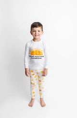 Young boy in Lovedbaby Organic Long Sleeve PJs, Sunny Day, smiling in eco-friendly, sun-themed PJs on a white background.