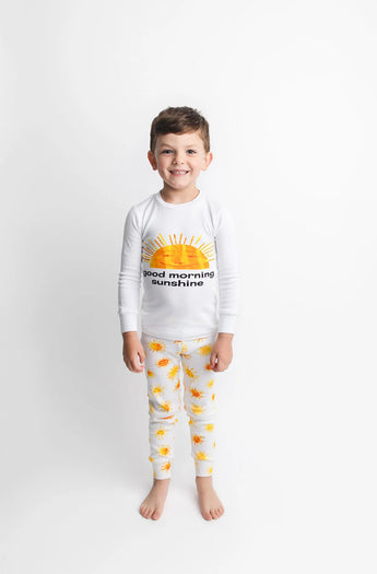 Young boy in Lovedbaby Organic Long Sleeve PJs, Sunny Day, smiling in eco-friendly, sun-themed PJs on a white background.