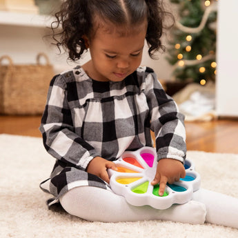 A child develops fine motor skills playing with a Dimpl Digits by Fat Brain Toy Co on a carpet, with a Christmas tree in the background.