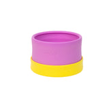 A purple/yellow silicone Essential Snack Bowl by morepeas, spill-proof lid, measures marked—ideal for adventures against a white backdrop.