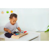 A child enhances coordination while joyfully playing with the PlanToys Musical Set, featuring a wooden xylophone and drumsticks.