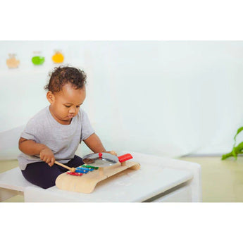 A child enhances coordination while joyfully playing with the PlanToys Musical Set, featuring a wooden xylophone and drumsticks.