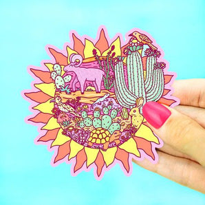 A hand displays Turtle Soups Vinyl Sticker, Desert Sun, featuring desert animals and a lizard on a bright blue background.