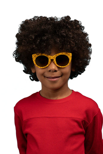 A child with curly hair wears Sunstaches Arkaid Sunglasses in Spongebob Pineapple style, red shirt, smiling on a white background.