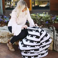 A woman sits on a stone ledge, draping a Milk Snob multifunctional cover with Disneys Mickey Mouse over an object, flowers blooming nearby.