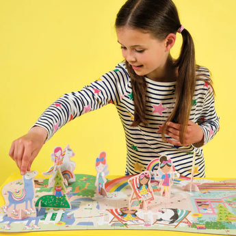 A girl in a striped shirt plays with the Floss and Rock 60 Piece Floor Puzzle, Rainbow Fairy on a sunny yellow backdrop.