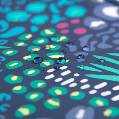 Close-up of water droplets scattered on a surface with a colorful abstract pattern. The pattern includes various shapes in green, yellow, turquoise, and white against a dark blue background.