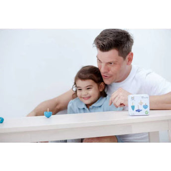 A man and child smile, enhancing fine motor skills with PlanToys sustainably made Spinning Tops at a table by a toy box.