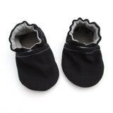 Cabooties Denim Black: Small black baby shoes with white stitching, ruffled edges, and flexible rubber soles on a white background.