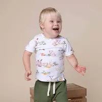 A joyful toddler in Snuggle Hunnys Organic T-Shirt, Farm stands near a cardboard box.