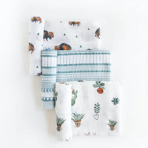 Set of three folded muslin swaddles by Little Unicorn with bison, geometric lines, and potted plants on white.