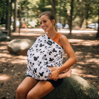A woman smiles outdoors with her baby in a Milk Snob Cover Disneys Mickey Sketch, perfect as a multifunctional car seat cover.