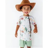 A young child in a Bird & Bean Billy set: large brown cowboy hat, a colorful cactus print shirt, and light green bamboo shorts, smiling.