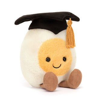 Jellycats Amuseables Boiled Egg Graduation is a plush toy with a smiling yellow yolk face, brown legs, and a cotton mortarboard.