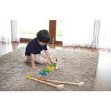 Child playing on a carpet with colorful blocks near PlanToys Mini Golf Set, wearing a navy shirt and beige shorts.