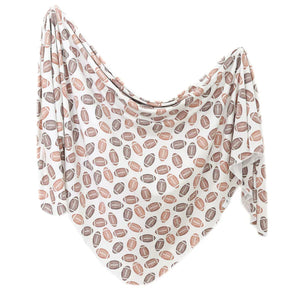 The Copper Pearl Knit Swaddle Blanket, Blitz, features modern designs with brown footballs on white fabric—ideal for a chic baby swaddle.