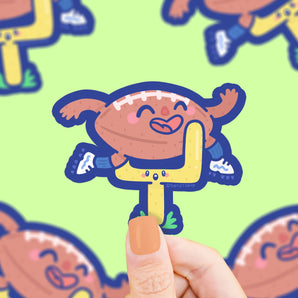 A Turtle Soup Vinyl Sticker shows a cartoon football character near a yellow goalpost on green, held by hand.