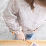 A child paints at an easel while wearing a Bumkins Long-Sleeved Art Smock: Wander, made of waterproof fabric.