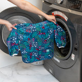 A person holds a Bumkins Long-Sleeved Art Smock: Animal Prints in front of an open front-loading washing machine.