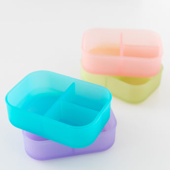 Four bento boxes, including a Bumkins Silicone Bento Box 3 Section: Blue Jelly, are arranged on a white background.