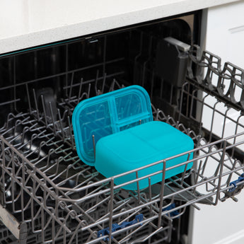 A bento box and lid from Bumkins Lunchbox Legends 6-Piece Set: Ocean Blue Jelly sit in the top rack of an open dishwasher.