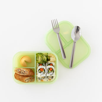 Bumkins Silicone Bento Box 3 Section: Green Jelly with spring rolls, sushi, cucumbers, and fortune cookie next to utensils on a white background.