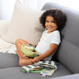 A curly-haired boy smiles, enjoying snacks with Bumkins Lunchbox Legends 6-Piece Set: Motley Green Jelly on a gray couch.