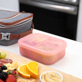 A bento box from Bumkins Lunchbox Legends 6-Piece Set: Disco Pink Jelly sits next to a lunch bag and a cutting board with fruit & meat.