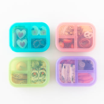 Four colorful bento boxes, including a Bumkins Silicone Bento Box 3 Section: Purple Jelly, filled with snacks on a white background.