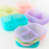 Bumkins Silicone Bento Box 3 Section: Purple Jelly sits among other similar bento boxes on a white background, their lids stacked.