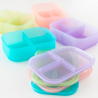Bumkins Silicone Bento Box 3 Section: Purple Jelly sits among other similar bento boxes on a white background, their lids stacked.