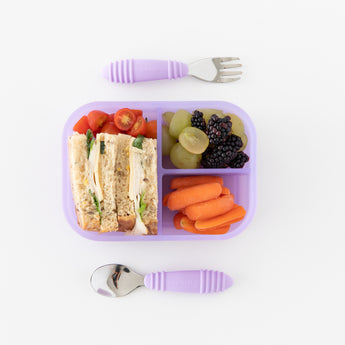 Bumkins Silicone Bento Box 3 Section: Purple Jelly holds a sandwich, fruit, and veggies on a white background with utensils on the side.