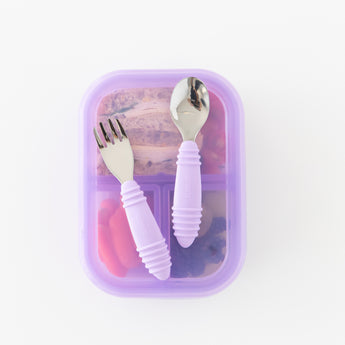 Bumkins Spoon + Fork: Lavender sits atop a purple bento box filled with food on a white background.