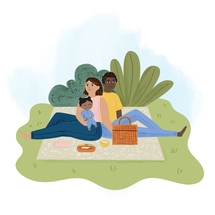 Illustration of a family on a picnic. A man, woman, and child sit on a blanket with a picnic basket. Trees and bushes are in the background. The child is wearing blue clothes and hugging the woman.